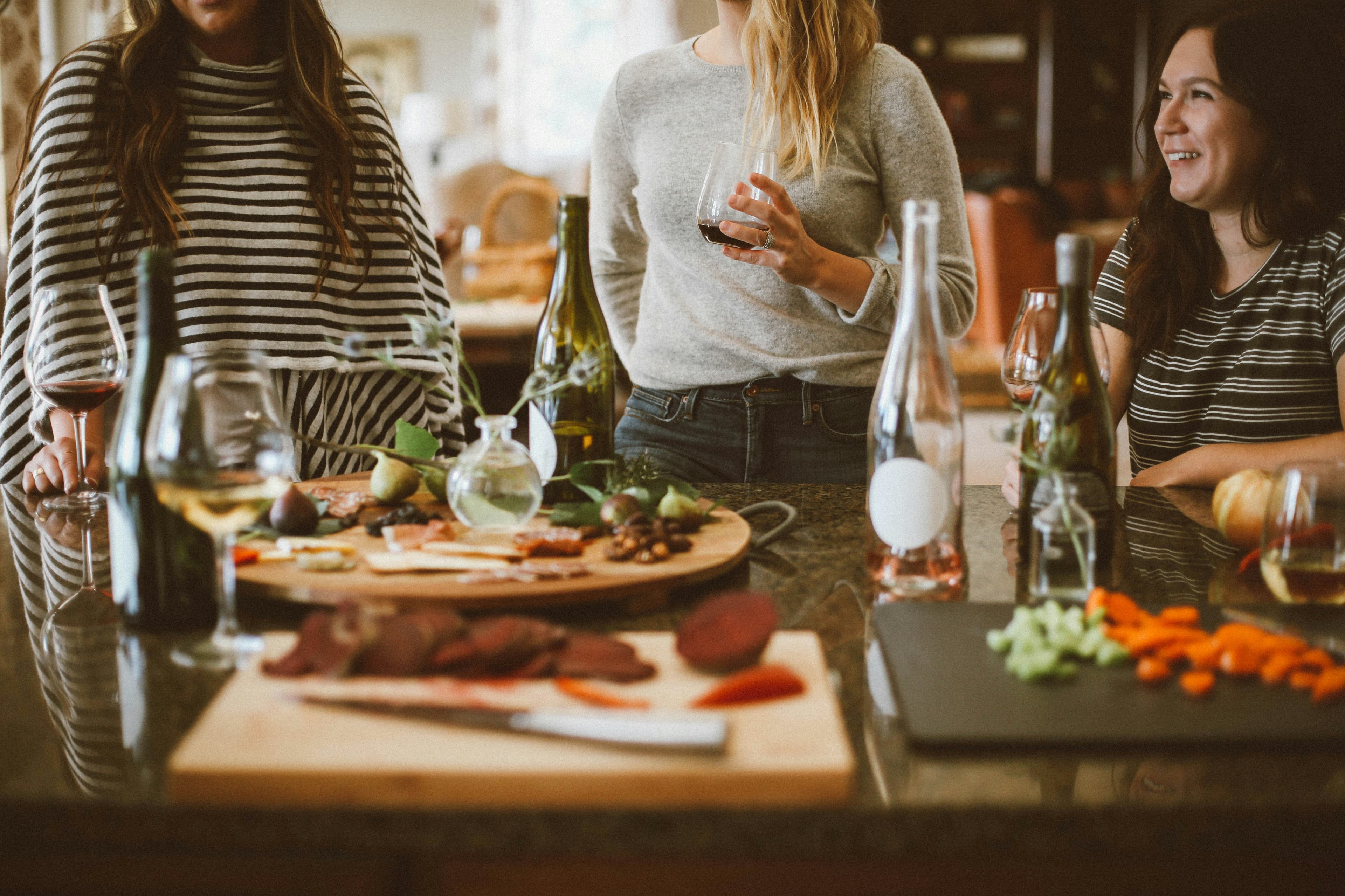 Trois amies autour d'une cuisine, verres de vin à la main, plateau de charcuterie devant elles