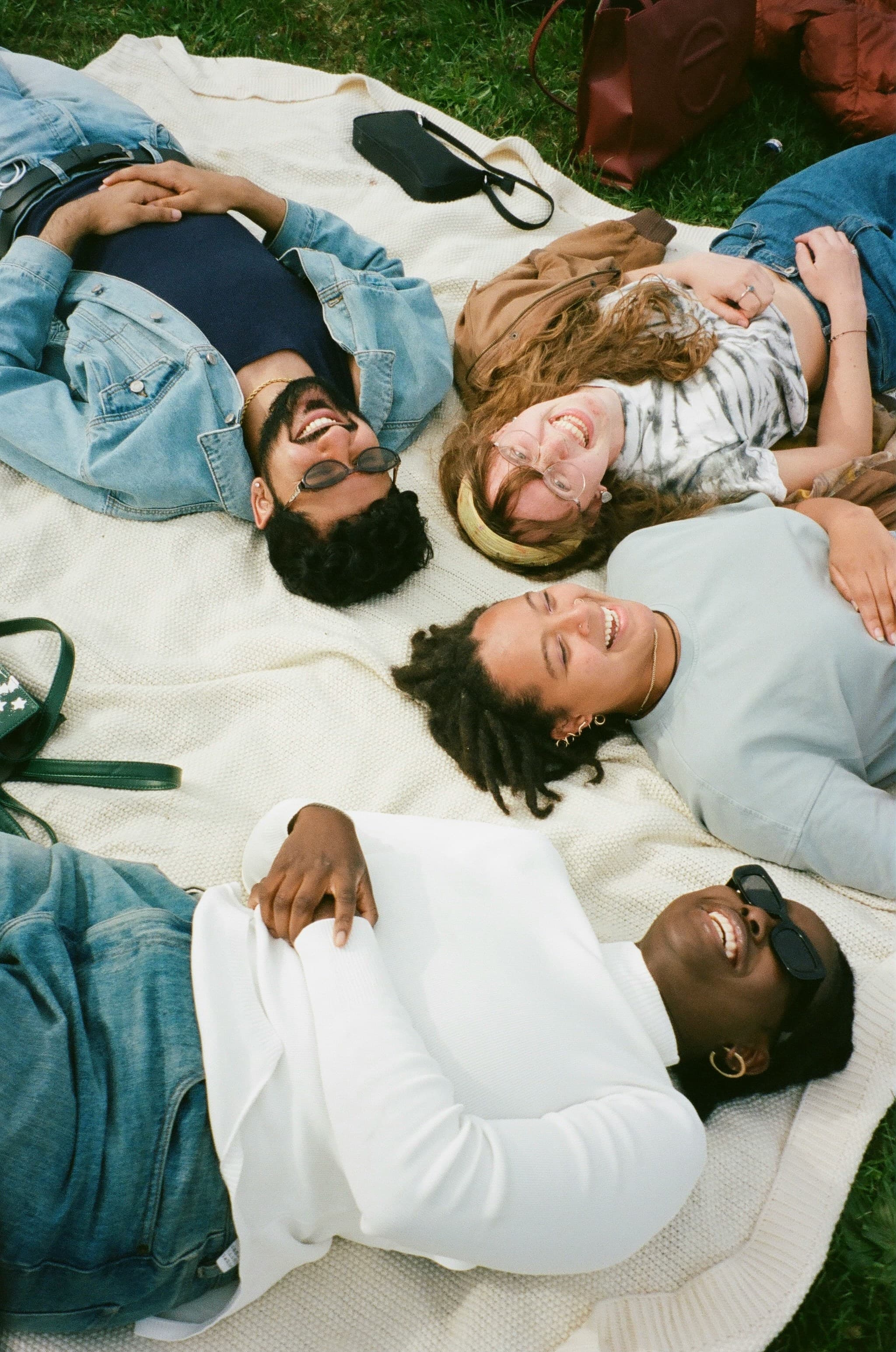 Quatre amis allongés en cercle sur une couverture, vus du dessus, riant ensemble